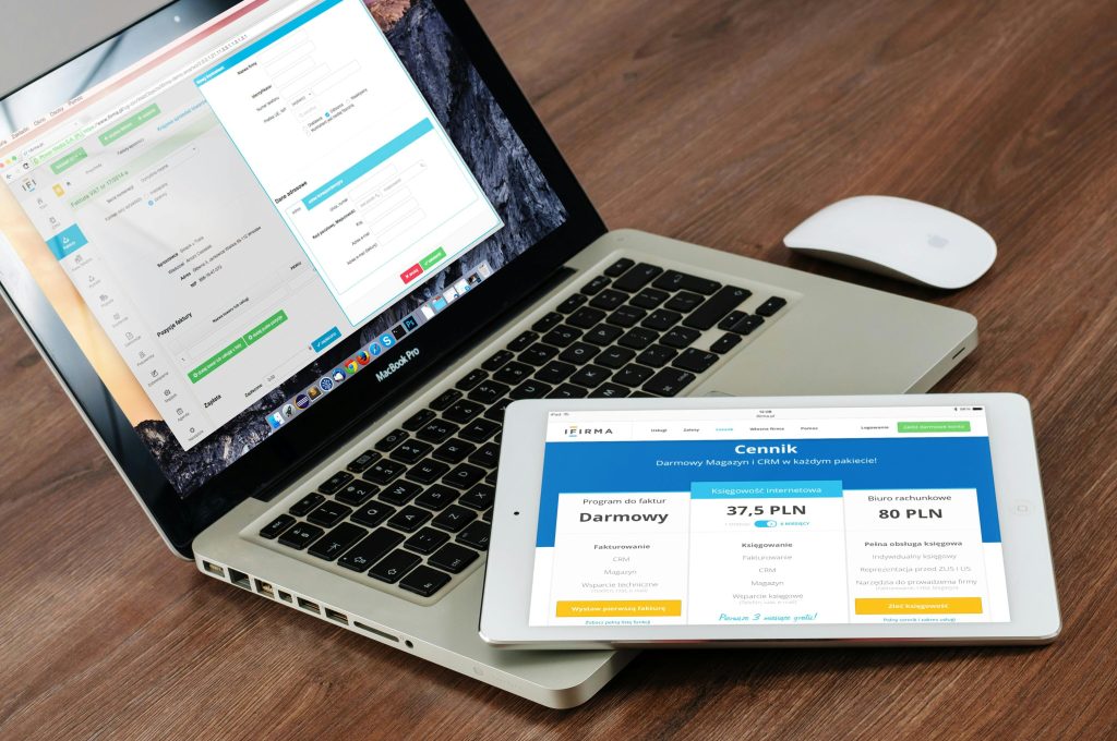 Ordinateur portable MacBook affichant une interface de gestion d'entreprise avec facturation et données client, accompagné d'une tablette présentant un site e-commerce avec tarifs de services en polonais, idéal pour illustrer les solutions numériques pour l'e-commerce artisanal.